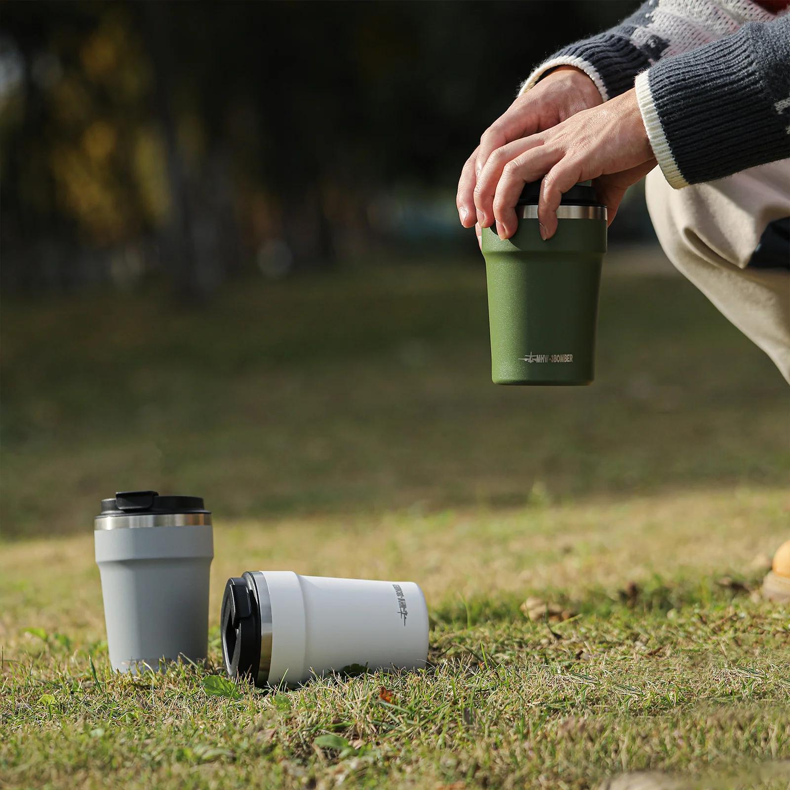 Person holding a green insulated mug with two other mugs on grass