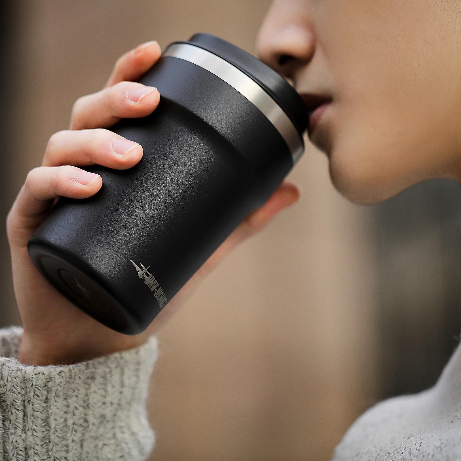 Person holding a black insulated mug with a blurred background