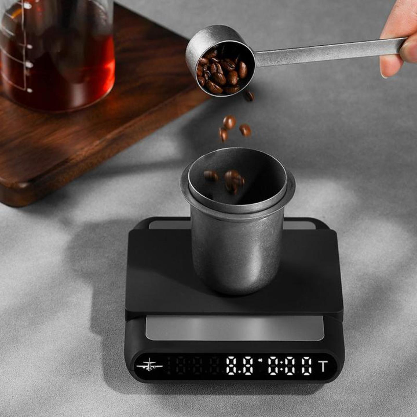 Coffee beans being poured into a coffee filter on a digital scale with a wooden tray and glass container in the background.