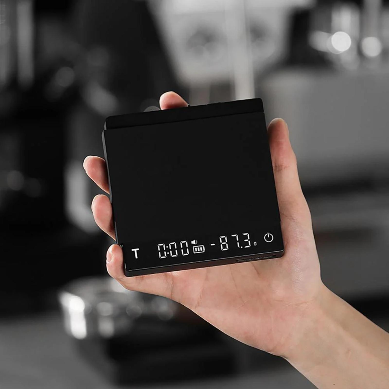 Hand holding a small black digital device with a blurred background