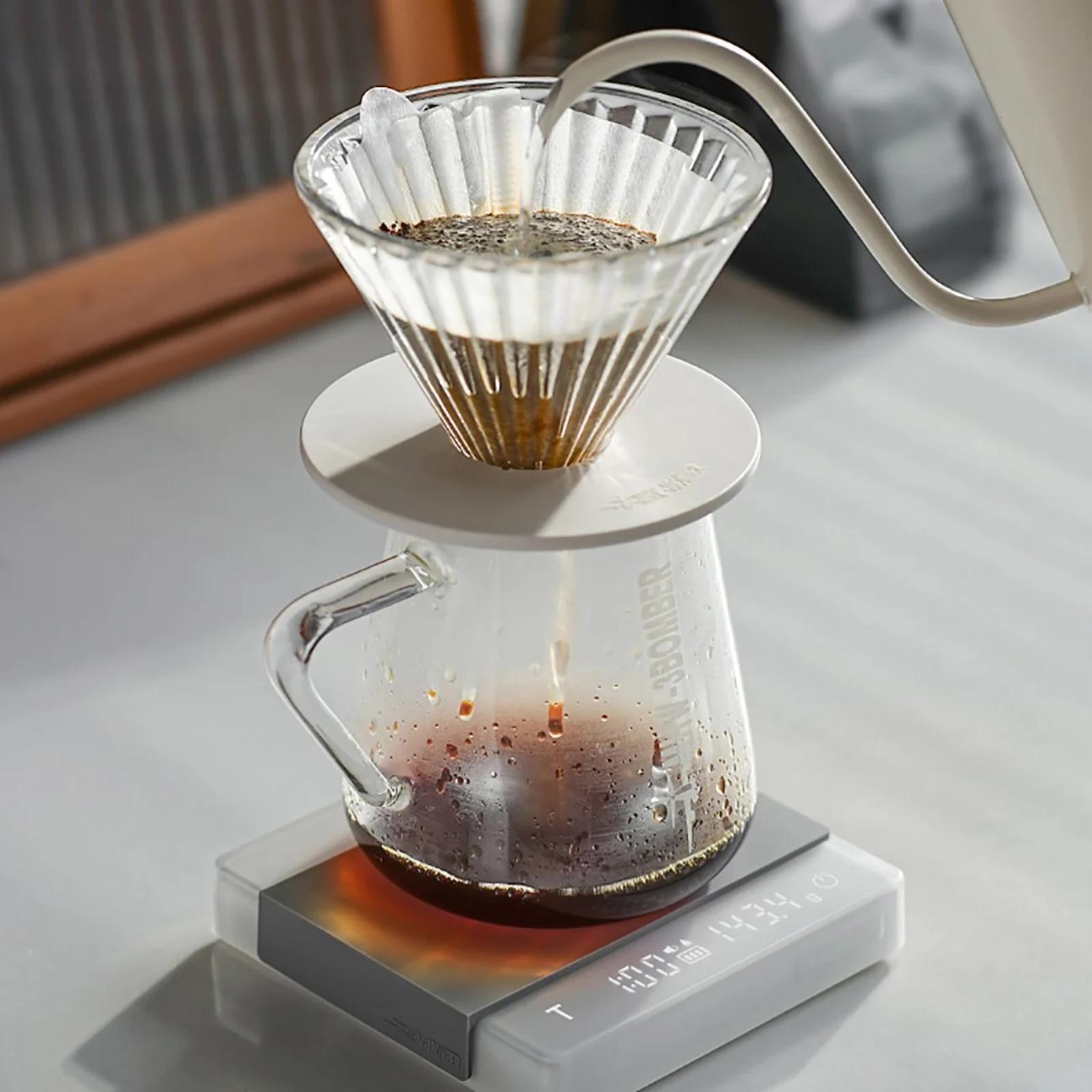 Coffee brewing process with a glass carafe and filter on a digital scale.